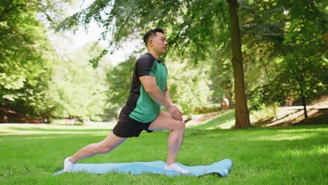 asian man performs gymnastics stretching practicing yoga warrior pose on mat in urban city park