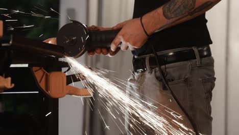 tough man with tattoos using grinding tool on steel creating sparks