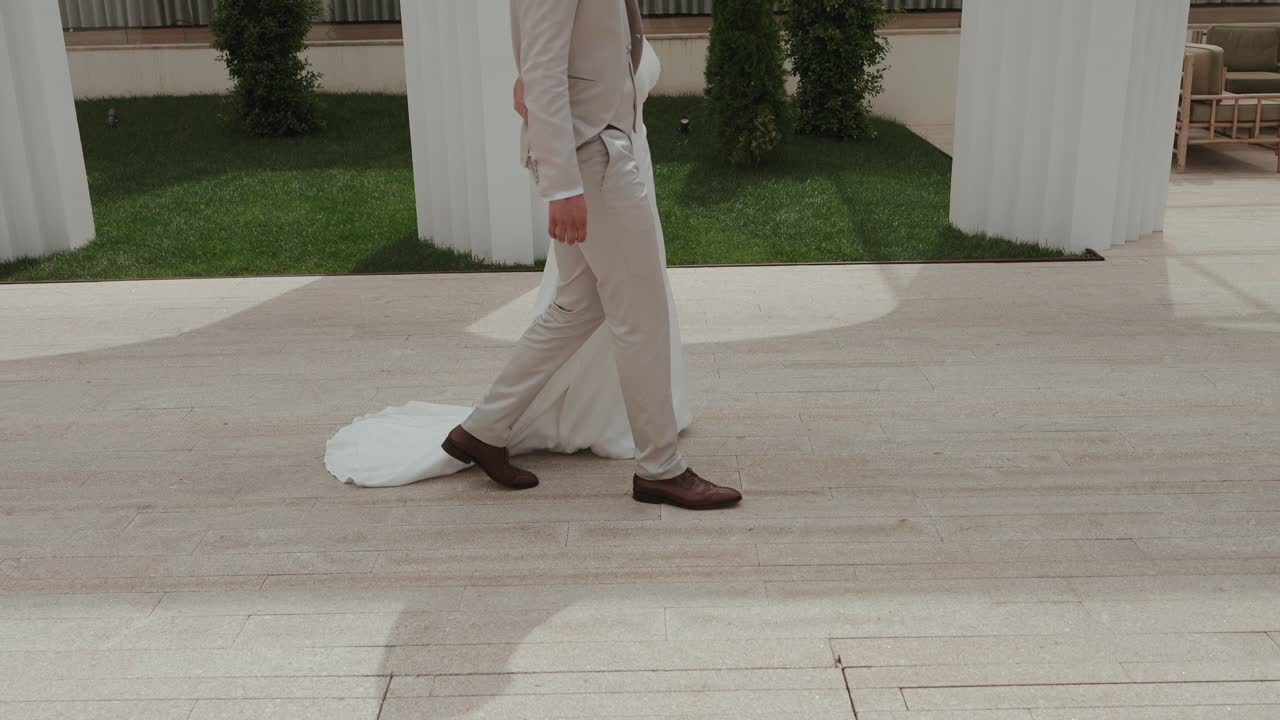 花嫁と花婿が並んで歩き、ウェディングドレスがアウトドアの小道で美しく揺れています。