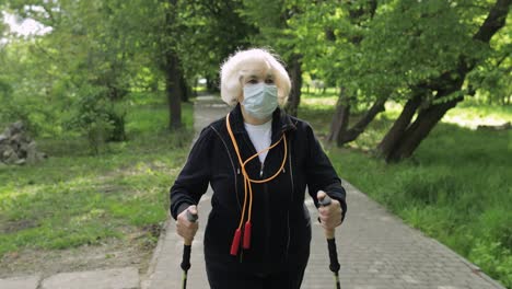 active senior old woman in mask training nordic walking in park at quarantine