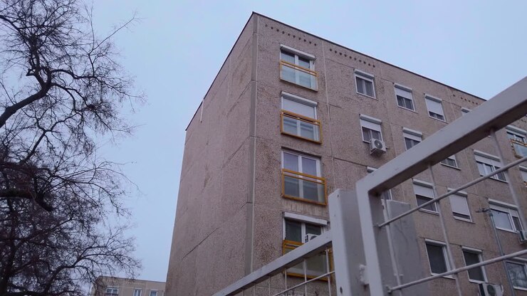 Prospettiva in prima persona che avanza su Tihamer utca a Budapest. Mostra condomini residenziali e alberi invernali spogli sotto un cielo pallido nel febbraio 2026. Autentico
