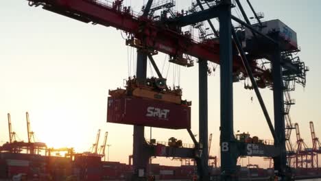 heavy machinery at a bustling shipping port operates during sunset, showcasing the loading and unloading of cargo containers by towering cranes against a vibrant sky.