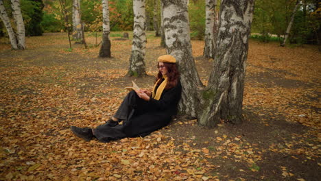 stylish lady sits in solitude leaning against tree, adjusting glasses while thoughtfully reading book, autumn leaves cover ground, surrounding peaceful forest setting