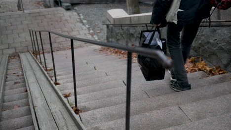 caucasian male homeless man walking with lots of bags down the stone staircase in a cold city, in slow motion