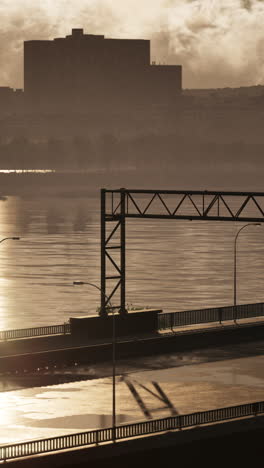 a bridge over a river in the city, with a large building in the background, at sunset