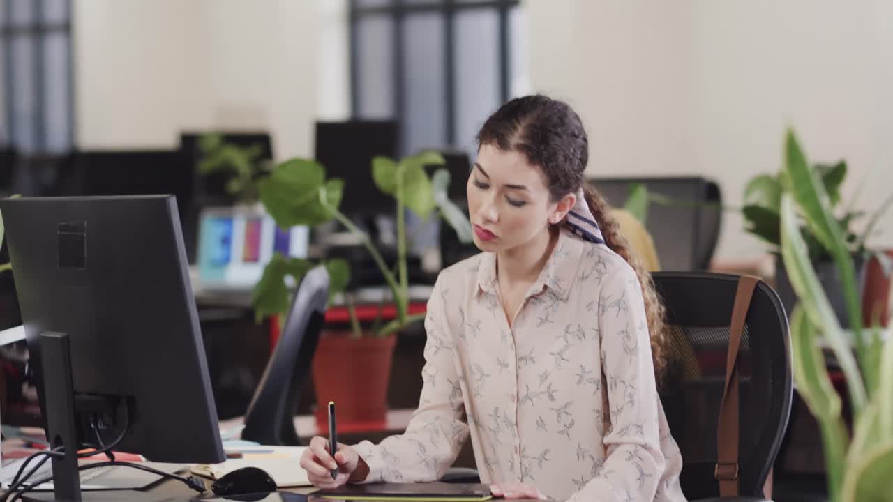 feliz mujer biracial creativa usando una tableta en una oficina casual, en cámara lenta