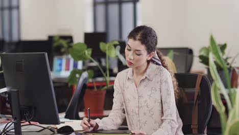 feliz mujer biracial creativa usando una tableta en una oficina casual, en cámara lenta