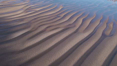 Antenne-Kreist-über-Einem-Wunderschönen-Strandsandrelief,-Das-Von-Meerwasser-Benetzt-Wird