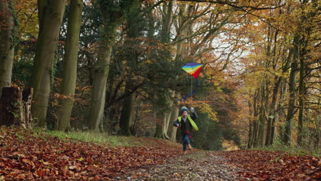 young boy having fun running along path through autumn countryside flying kite