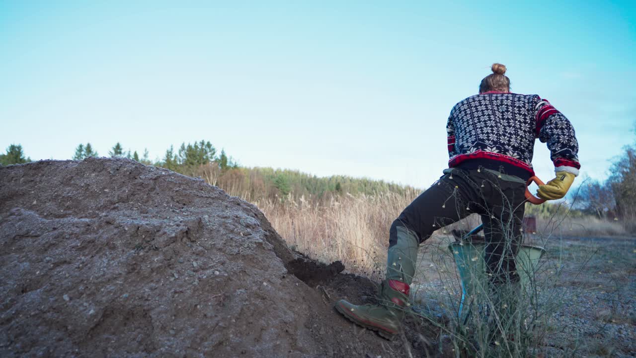 un hombre está excavando tierra y colocándola en un cubo para construir un invernadero - toma estática