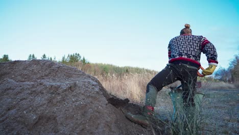 a man is excavating soil and placing it in a bucket for constructing a greenhouse - static shot