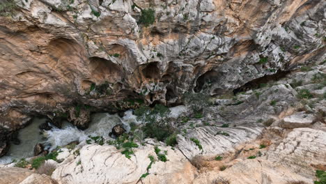 Toma-De-4k-De-Arriba-Hacia-Abajo-De-Un-Río-Frío-De-Montaña-Entre-Altos-Acantilados-En-El-Caminito-Del-Rey-En-Gorge-Chorro,-Provincia-De-Málaga,-España