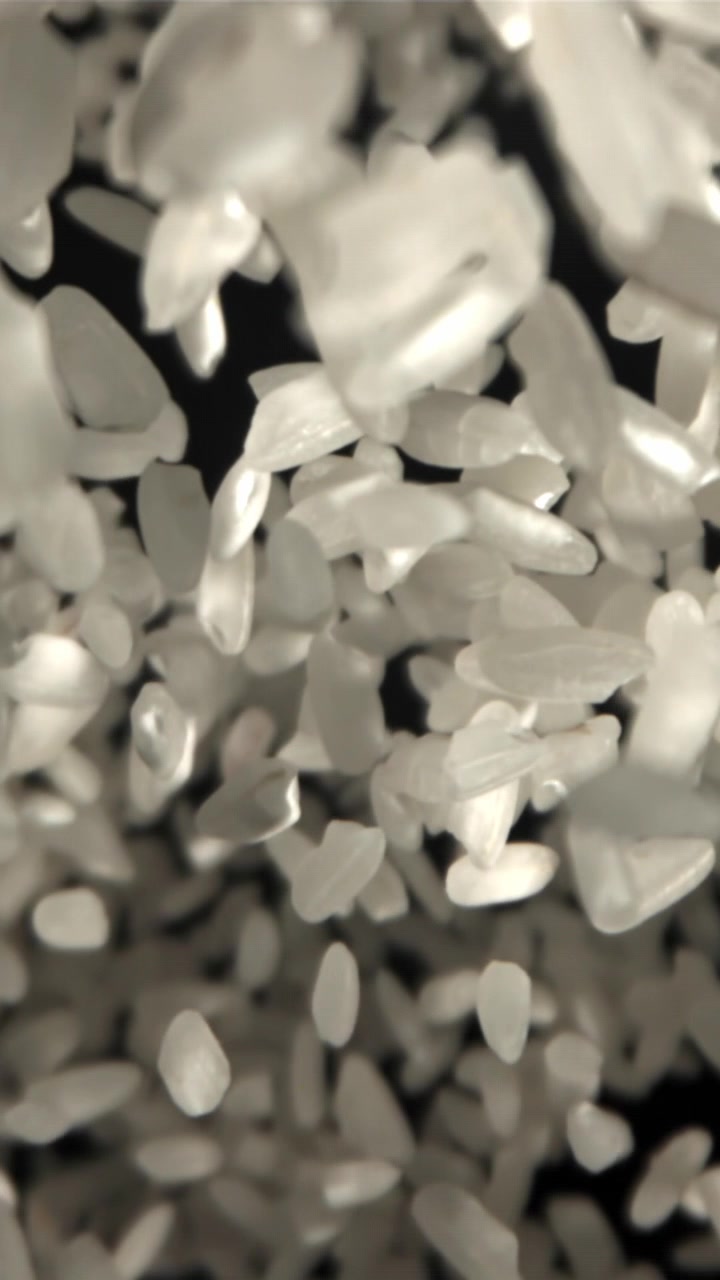Chicchi di riso bianco che cadono al rallentatore su sfondo scuro