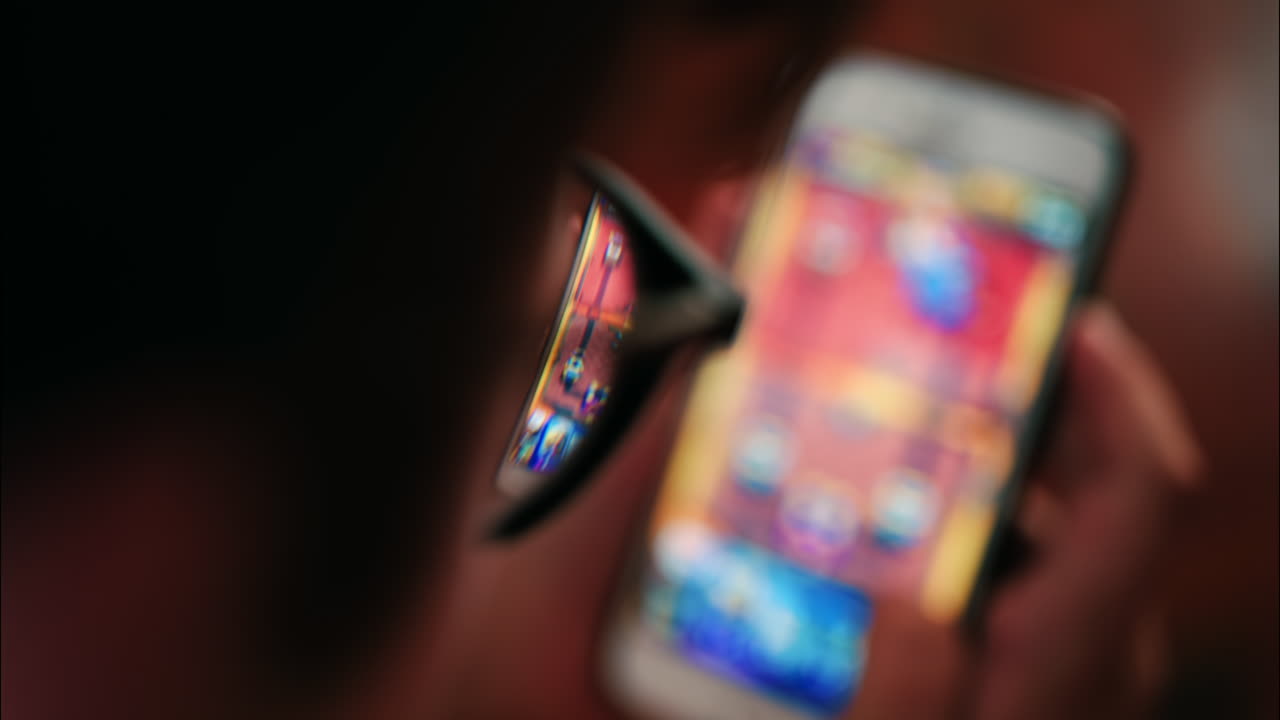 Over-the-shoulder close-up of a kid with glasses playing on a smartphone indoors