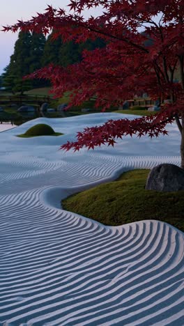 white sand ripples extend across a serene zen garden, accented by a vibrant red maple tree, small green mounds, rocks, and a tranquil pond reflecting the soft light of dawn