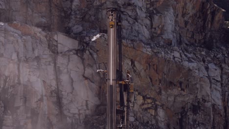 vertical drilling rig piercing through the rock face of a stark quarry cliff