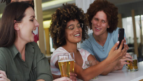 Diverse-group-of-happy-friends-drinking-beers-and-using-smartphone-at-a-bar