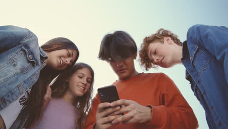 un grupo de adolescentes con dos chicas y dos chicos viendo algo divertido en la pantalla de un teléfono móvil