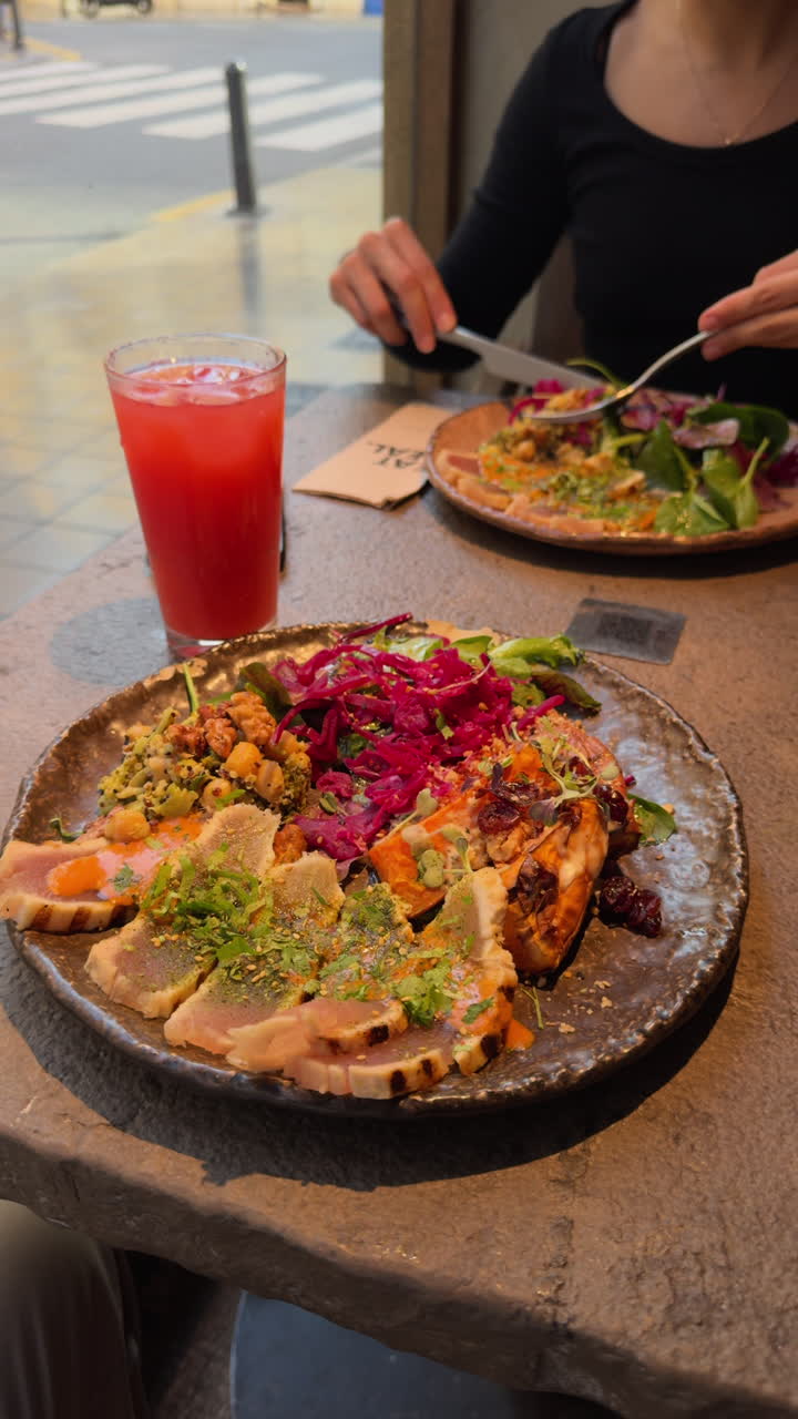 Healthy and delicious meal on a rustic plate in a restaurant. A woman is enjoying a fresh seared tuna tataki salad for lunch or dinner