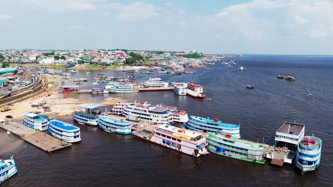 Aerial drone view of the busy harbor in Manaus, Brazil, showing passenger boats and ferries docked along the Amazon River with the city’s riverside buildings visible in the background
