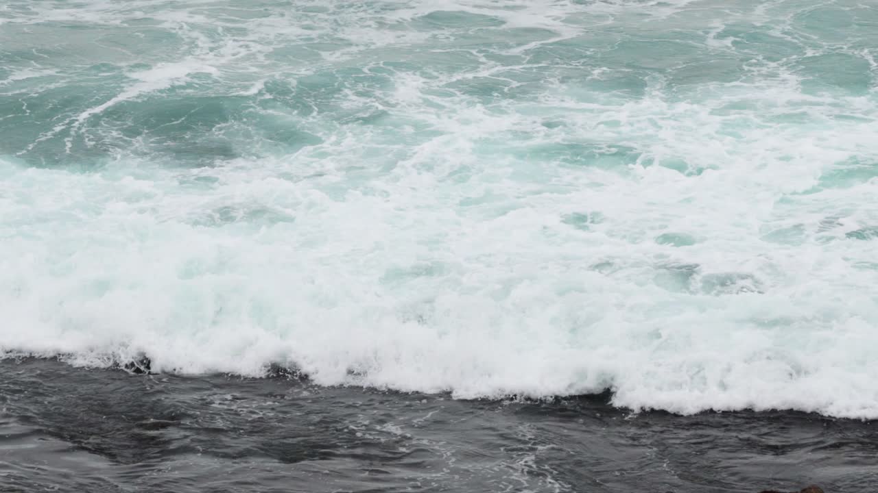 Dynamic ocean waves crash against the rocky shore, captured in natural lighting along Australia's scenic Great Ocean Road