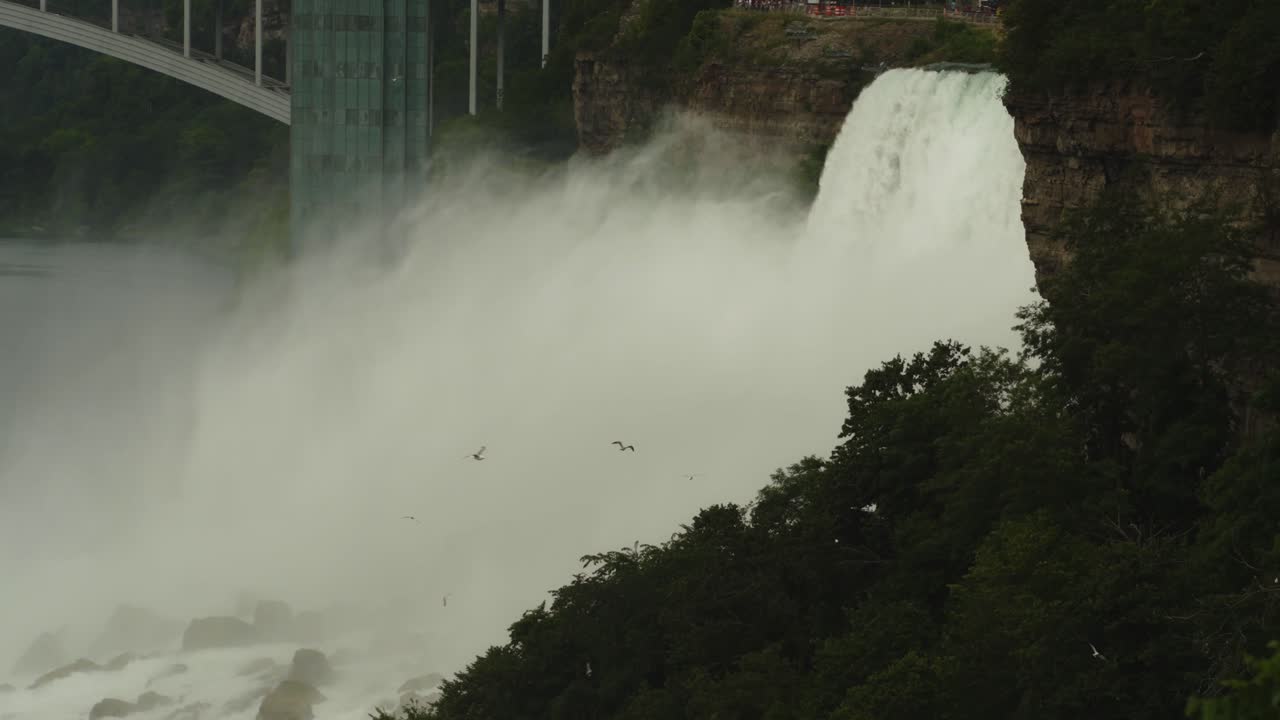 Thick mist rises from Niagara Falls with the Rainbow Bridge and Observation Tower looming above the gorge