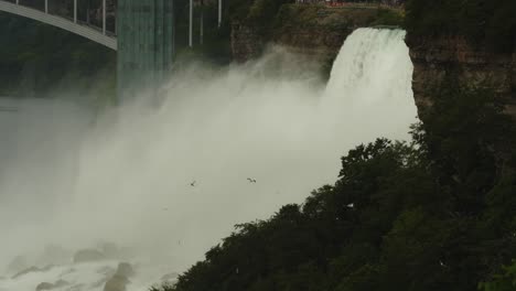 thick mist rises from niagara falls with the rainbow bridge and observation tower looming above the gorge
