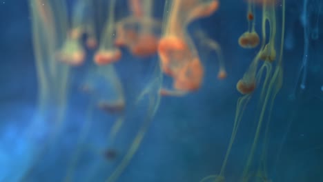 abstract figures of orange liquid moving down in dark blue water