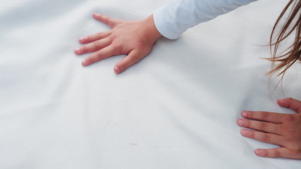 피크닉 준비 중 십 대 소녀가 푸른 잔디 위에서 흰 천을 부드럽게 펼치는 모습의 항공 뷰로, 은은한 움직임, 부드러운 텍스처, 자연광으로 가득 찬 고요한 야외 분위기를 보여줍니다.