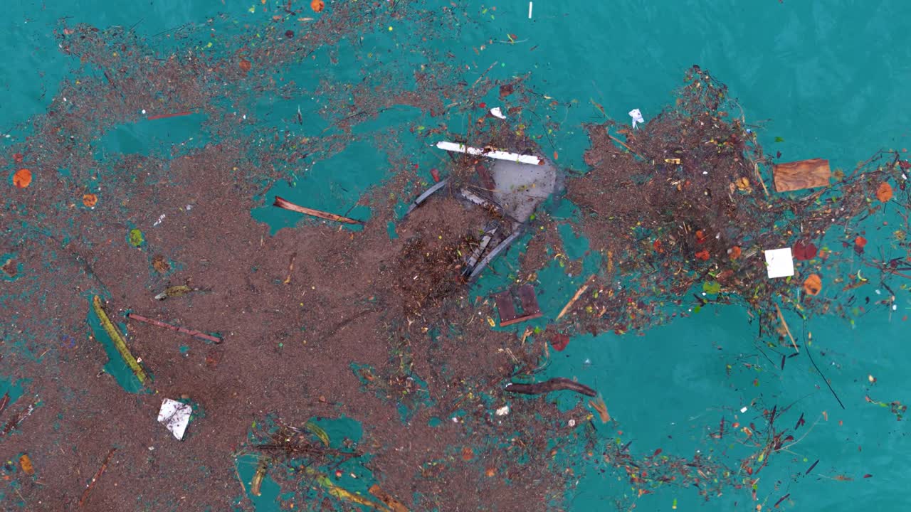 vista general de arriba hacia abajo de la silla de playa de plástico rota y los escombros frondosos naturales que flotan en el agua del océano