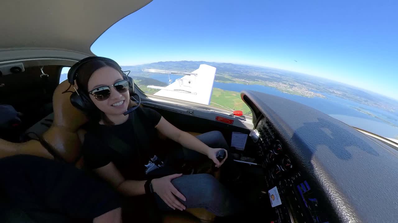 선글라스를 쓴 젊은 여성 파일럿이 작은 개인 비행기를 타고 주위를 둘러보며 웃고 있습니다.
