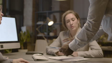 close up view of unrecognizable american man employee holding a tablet and explaining a project to female coworkers who are sitting at desk in the office