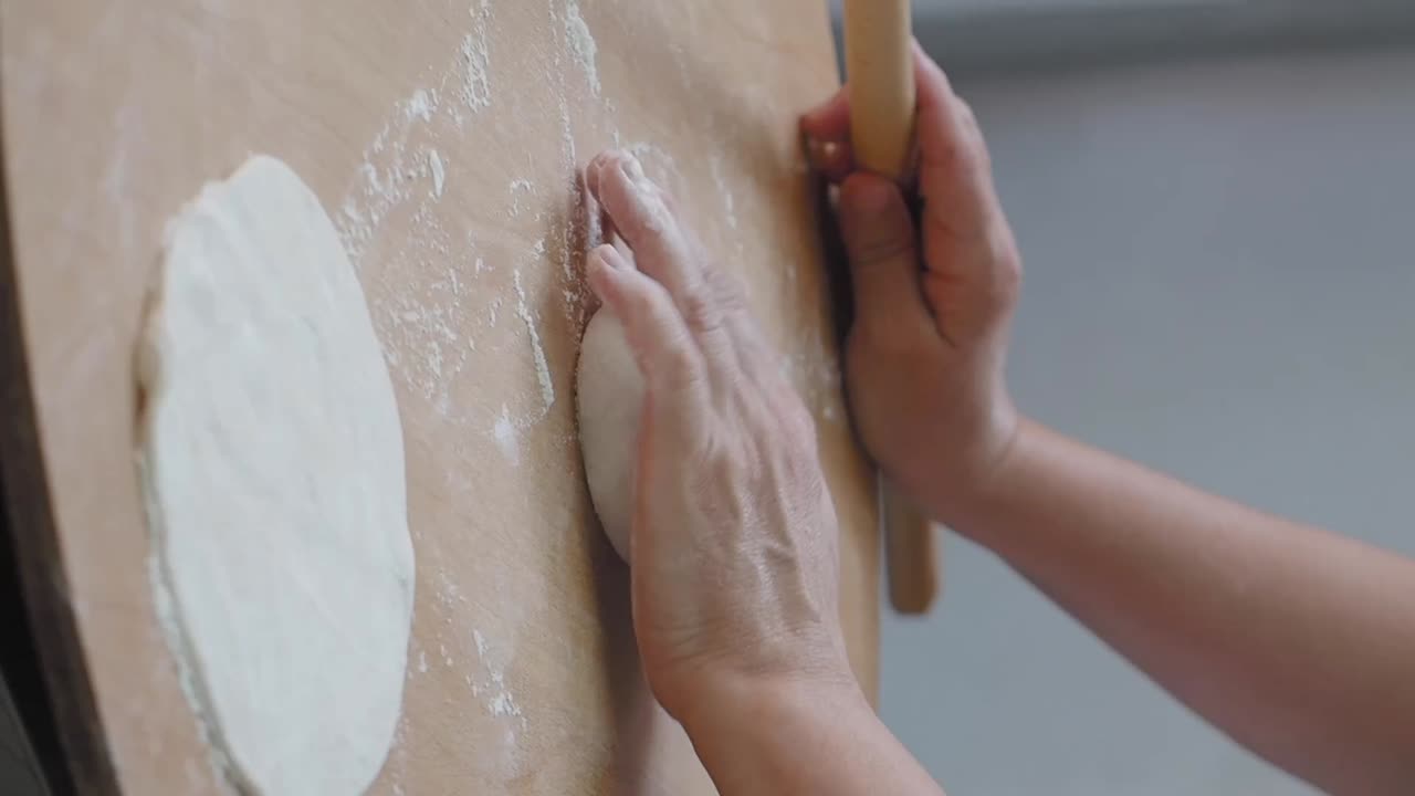 Hands preparing dough with a rolling pin