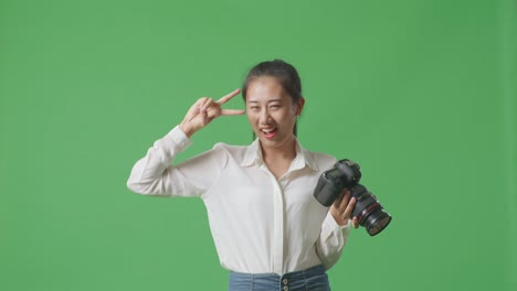 asian photographer looking at the pictures in the camera then screaming goal and dancing celebrating finishing her work while standing on green screen background in the studio