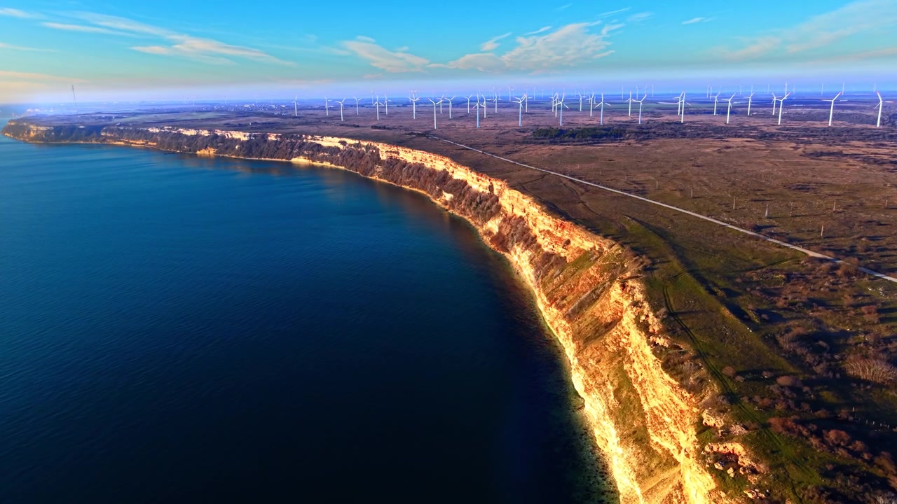 Vista aérea de falésias de calcário e parque eólico ao longo da costa do Mar Negro. Perspectiva elevada de promontório curvo e erodido com face rochosa ocre margeando águas azuis profundas, turbinas brancas no planalto acima