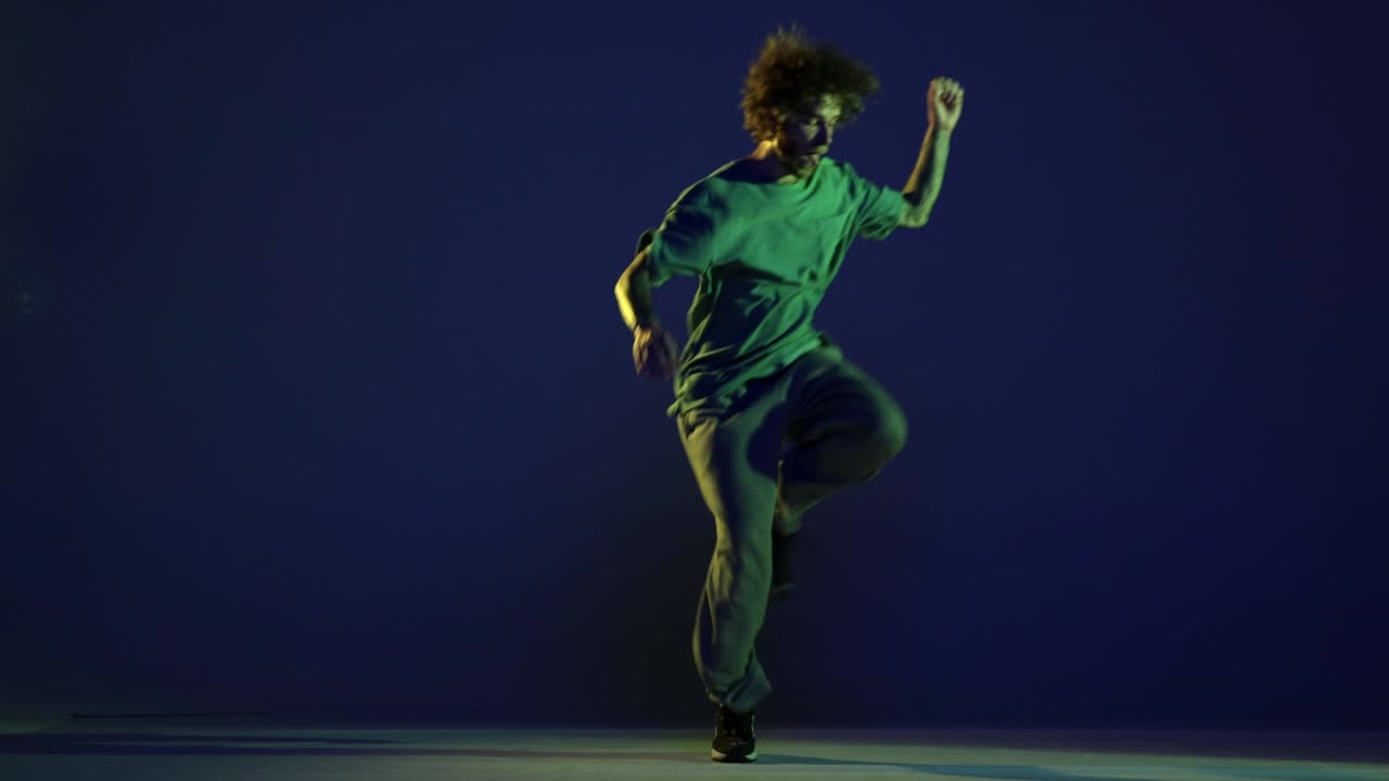 Stylish young man, hip-hop dancer dancing isolated over dark blue background in neon light. Modern dance art, fashion, youth, ad, style. 4K, video
