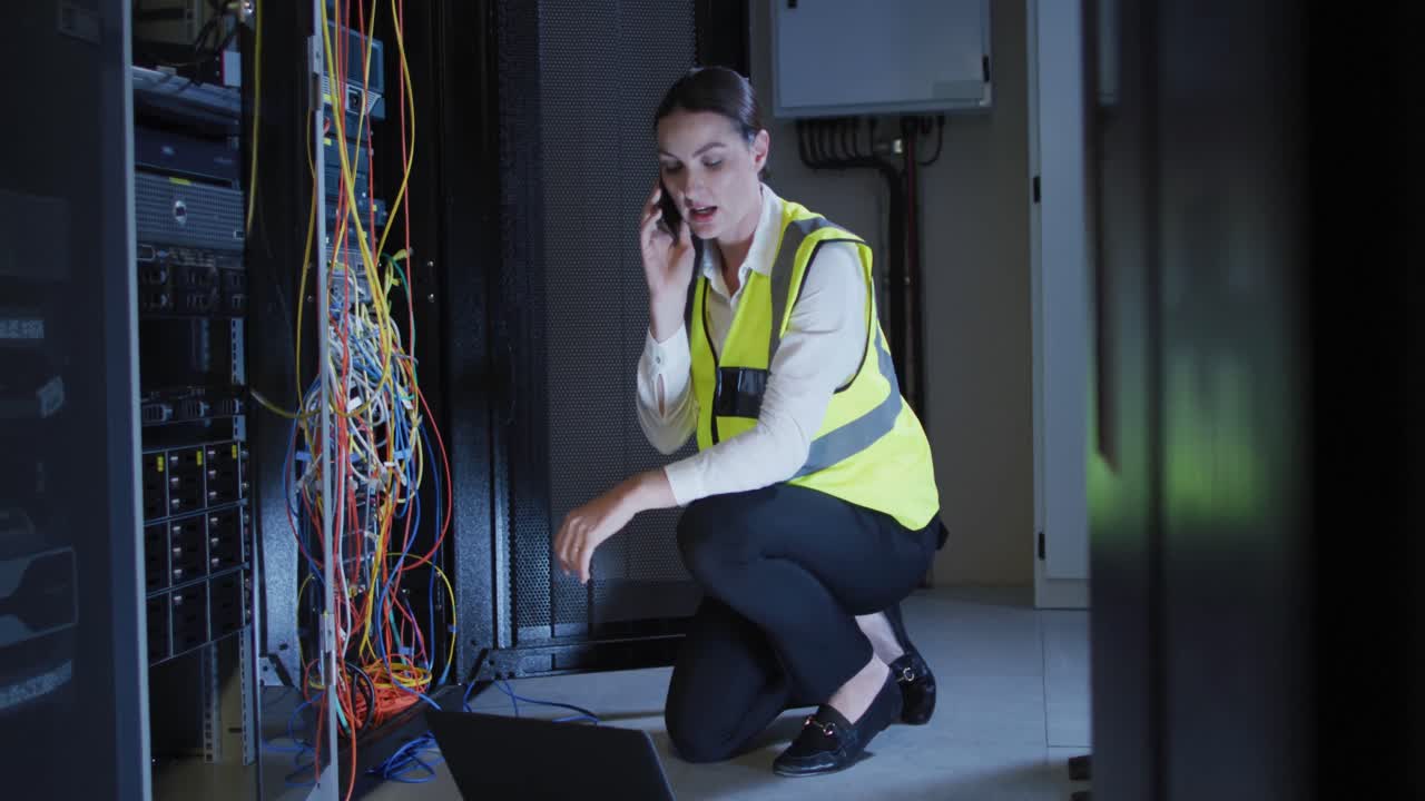 Caucasian female it technician using smartphone and laptop checking computer server