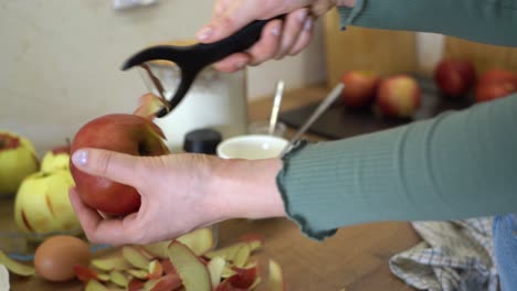 un primer plano de las manos de una mujer, pelando una manzana roja con un pelador