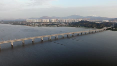 Hong-Kong-Shenzhen-Bay-Bridge-with-Tin-Shui-Wai-buildings-in-the-horizon-and-Fish-and-Oyster-cultivation-pools,-Aerial-view