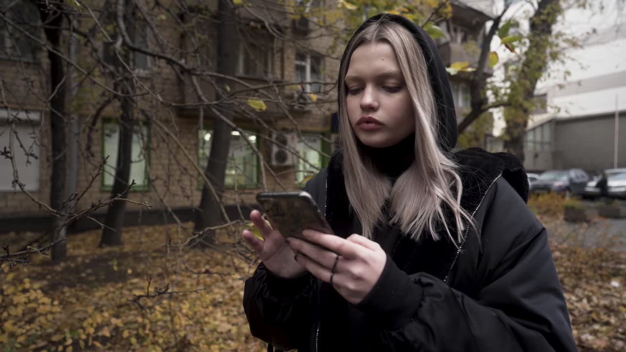 молодая женщина переписывается по смартфону в осеннем городе.