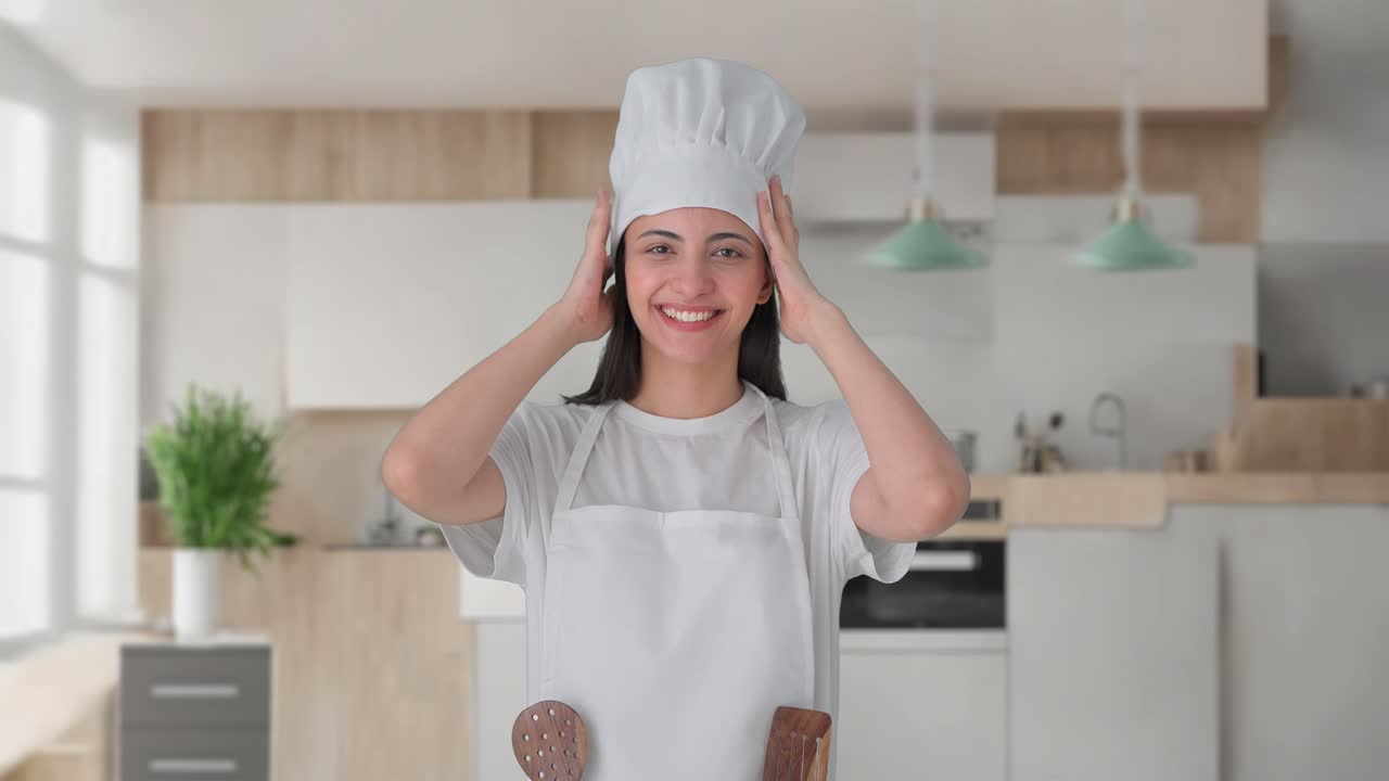 Cuoca professionista indiana felice che indossa un cappello e un grembiule