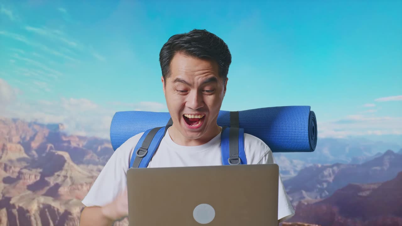 Close Up Of Asian Male Hiker With Mountaineering Backpack Looking At A Laptop And Screaming Goal Celebrating The Success While Traveling At The Top Of Mountain