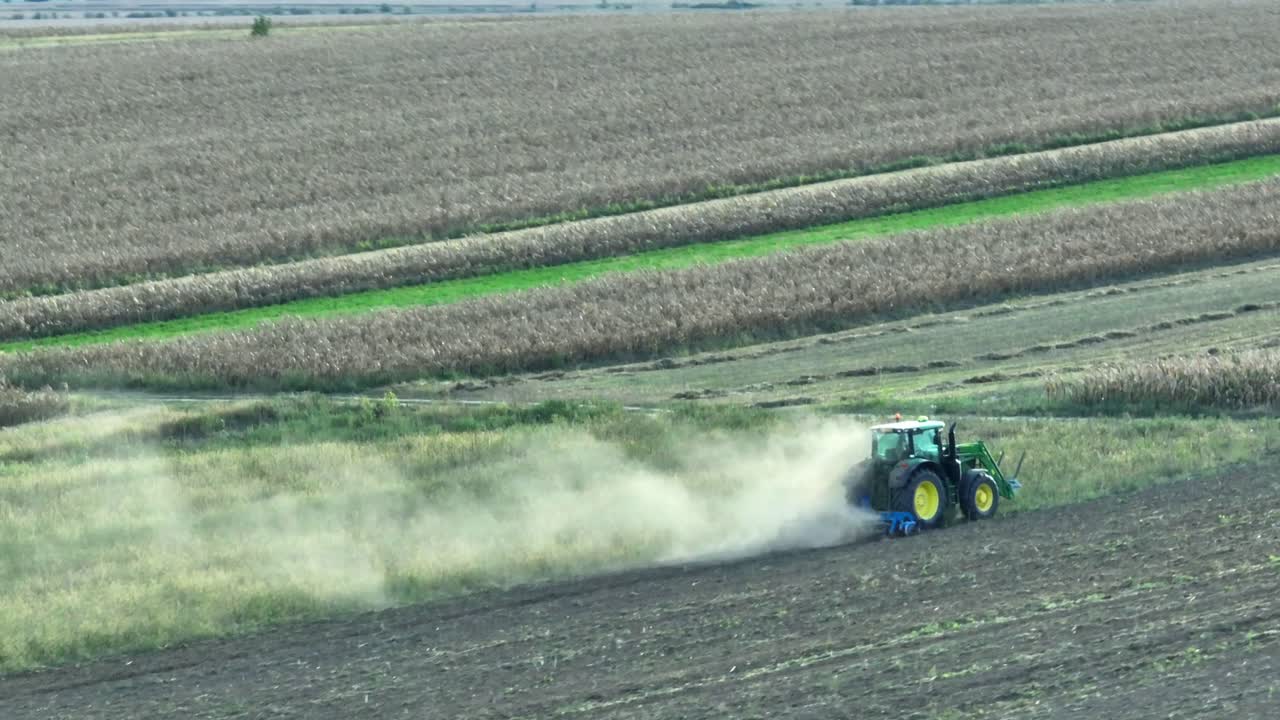 Ripresa cinematografica con drone di un trattore che ara un campo agricolo con polvere che si alza durante una giornata nuvolosa in una zona rurale della Romania