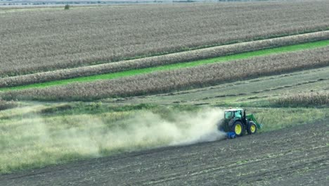 Cinematic-drone-shot-of-tractor-plowing-agricultural-field-with-rising-dust-during-cloudy-day-in-rural-area-of-Romania