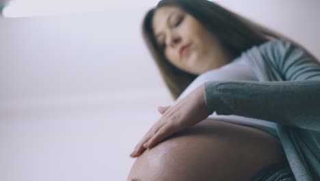 pregnant woman in casual clothes applies cream on belly