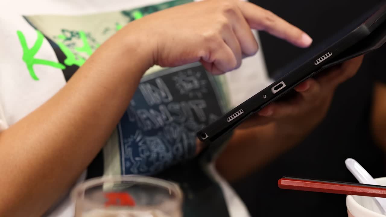 A person points at a tablet screen, surrounded by dining items on a table.