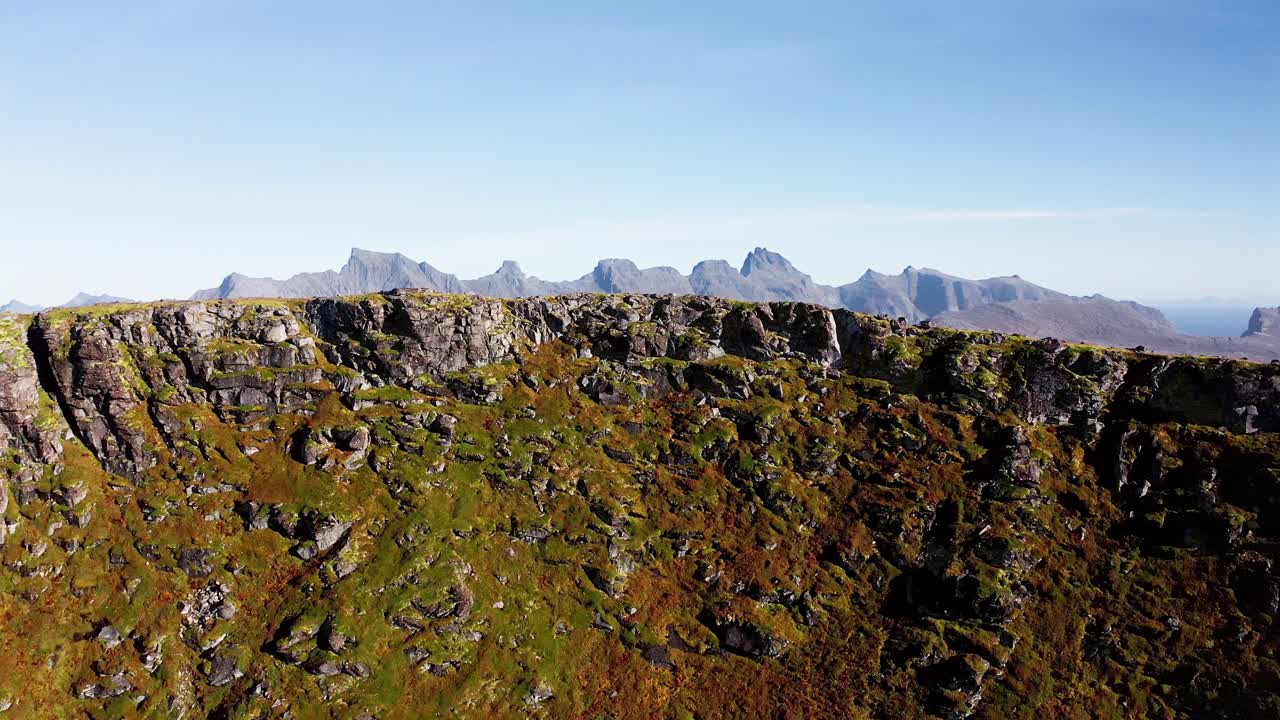 revelación de una magnífica cadena de montañas detrás de un majestuoso acantilado en un pájaro azul día de cielo despejado en el, cerca de la playa de kvalvika, islas loftoten, noruega