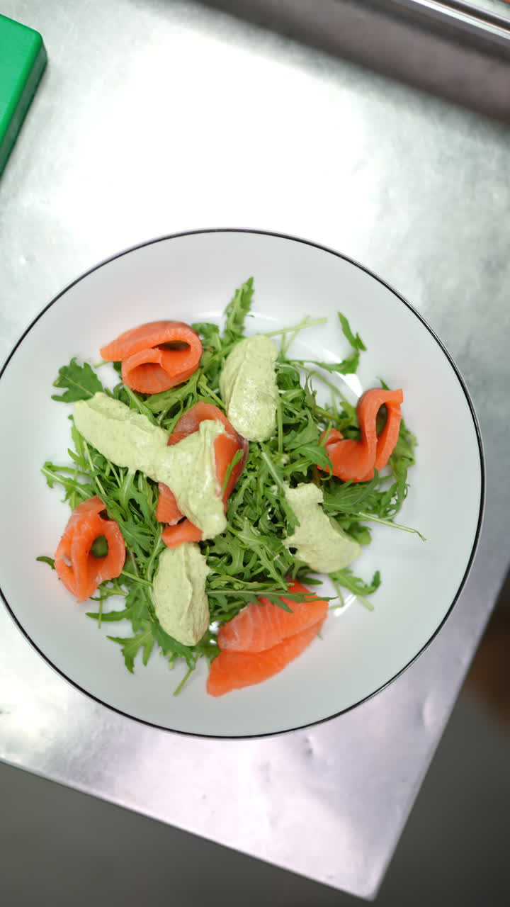 Vertical footage Professional chef carefully sprinkling crispy croutons over colorful salmon salad with creamy avocado spread and fresh arugula leaves in modern restaurant kitchen workspace