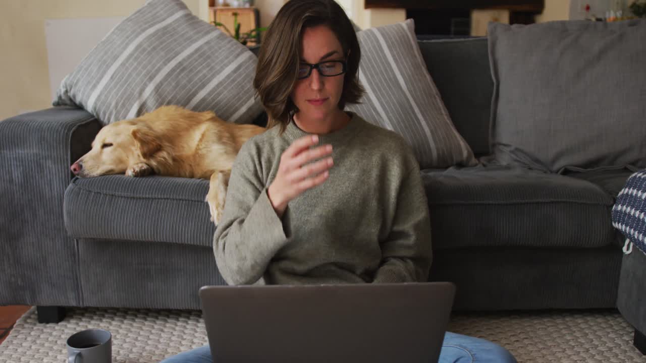 Caucasian woman using laptop working from home with her pet dog on sofa next to her