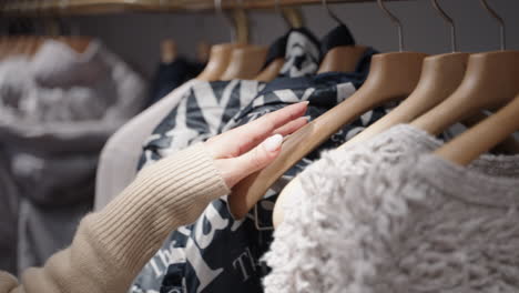 primer plano de la mano de una mujer pasando por la ropa en una tienda de ropa